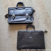 Top view of two black leather briefcases, one featuring front buckle pockets and an embossed logo on the other