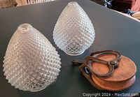 Two vintage glass globe shades with diamond texture and one wooden pulley on a dark surface.