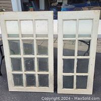 Front view of two wooden window frames, each with multiple glass panes, one painted cream and one stripped paint.