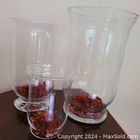 Front angle view of 3 clear glass hurricane vases with amber glass beads inside, arranged by size.