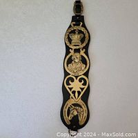 Full view of 4 antique brass horse brasses mounted on black leather strap with buckle.