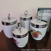 Four egg coddlers: two decorated Royal Worcester coddlers and two plain white large coddlers all with silver-tone lids.