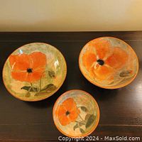 Top view of three pottery bowls with peach poppy flower paintings, showing colors and design details.