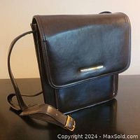 Front and side view of the brown leather cross-body purse placed on a dark surface showing smooth leather and adjustable strap.