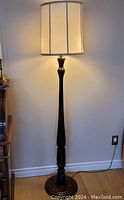 Front view of vintage solid wood floor lamp lit with custom off-white lamp shade, showing elegant turned wood base and body.
