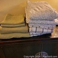 Stack of three folded flannel sheet sets on a dark wooden surface, including green solid color and patterned sets.