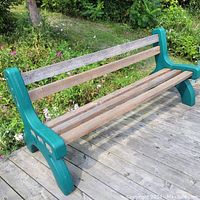 Green plastic outdoor bench with cedar wood slats showing front and side views on wooden deck beside garden flowers.