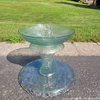 Full view of the green translucent glass birdbath showing embossed patterns on the base and bowl, with a bird figurine at the center.