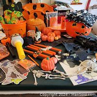 Overview of lot showing orange pumpkin bucket, small pumpkins, skeletons, bats, and assorted Halloween decorations on black tablecloth