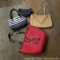 All three handbags displayed on carpeted floor: large red straw handbag, natural straw handbag, and smaller reversible black and white handbag