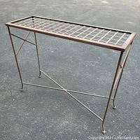 Side angled view of metal outdoor console table with grid top on asphalt surface.