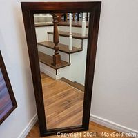 Full view of the rectangular wall mirror leaning against a wall, showing the wood frame and clear reflective surface.