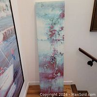 Full view of tall narrow acrylic painting leaning against a wall in a corner.