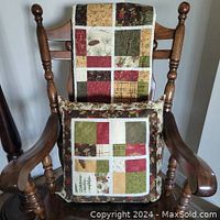 Quilt and pillow displayed draped and resting on wooden chair, showing patchwork block design in festive colors