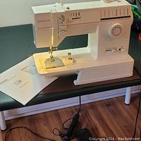 Full side view of the Singer Model 9015 sewing machine with included manual placed alongside, power cord and foot pedal visible beneath table.
