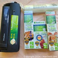 Sunbeam 2200 Series FoodSaver vacuum sealer unit with accompanying FoodSaver branded heat-seal rolls and bags on table.