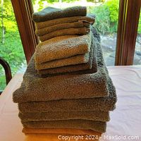 Stack of six bath towels including four green and two brown towels arranged on a table in natural light.