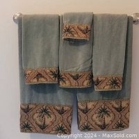 Green towels displayed on a towel rack showing palm tree patterned border on the edges of 2 bath towels, 4 hand towels, and 1 facecloth.