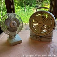 Two small oscillating fans placed on a table, one traditional desk style and one portable fan with handle.