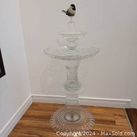 Full view of the upcycled glass birdbath showing its height and base on hardwood floor against a wall.