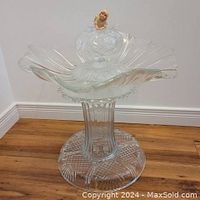 Full view of upcycled glass birdbath standing on wooden floor, featuring large wavy petal-shaped basin and pedestal base.