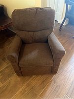 Children's recliner chair in textured brown upholstery fabric, showing front view in upright position on wooden floor.