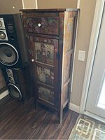 Full view of wooden country-style hutch with grape motif, mesh front door, drawer, and white knobs, placed on dark wood floor near wall.