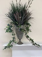 Full view of custom silk plant arrangement approximately 24 inches tall with green ivy, tall grass, and brown cattail-like stems in a decorative metal footed pot against a light wall background.