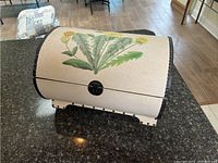 Curved table top storage bin with floral decor on black countertop.