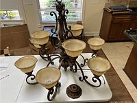 Large heavy metal chandelier with 8 curved arms and cream marbled glass bowls for lights on a table indoors.