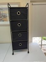 Black 4 drawer rolling storage unit with fabric drawers and metal grommet handles on caster wheels.