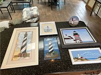 Overview of six lighthouse-themed picture frames and one decorative plate on a dark countertop.