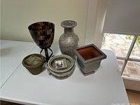 Five indoor flower pots and vases of various shapes and materials displayed on white surface near window