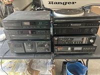 Photo of a collection of vintage stereo components stacked on a table with cords visible, including Pioneer and Sony brands, featuring CD players, turntable, cassette decks, equalizer, and stereo receiver.