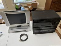 Photo shows an off-white Sony CRT monitor on left and a black multi-component stereo system on right with stacked audio components, plus an audio cable coiled in front.