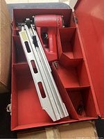 Red pneumatic nail gun in metal red storage box