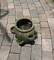 Photo of green ceramic planter with multiple small spouts on a paved outdoor ground.