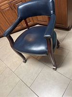 Blue leather rolling armchair featuring wooden curved legs and arms with brass nailhead trim. Photo focuses on seat and armrest showing overall condition.