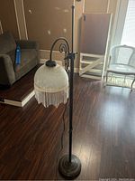 Photo showing the vintage floor lamp standing on a dark hardwood floor next to furniture, highlighting the curved metal arm and beaded glass shade.