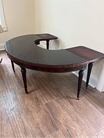 Photo showing the vintage horseshoe shaped table with black top, folded down ends, and legs on wheels