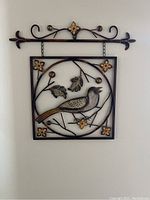 Photo of square metal wall art with bird and floral design hanging on wall.
