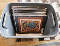Grey plastic bin filled with prints in clear sleeves showing front print with abstract design featuring blue oval and brown border