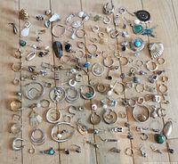 Layout of 150 single earrings on wooden surface showing a wide variety of designs and styles including hoops, studs, dangles, and unique decorative pieces.