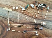 Photo displaying 16 vintage hat pins, showing a variety of decorative tops including cameos, floral motifs, enamel, and metal designs on a wooden surface.