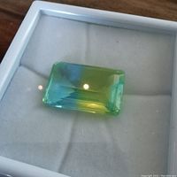 Top-down view of emerald-cut bi-colour tourmaline in white display tray showing colour and cut