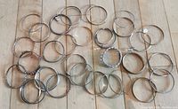 Top-down view of 32 assorted silver tone bangle bracelets laid out on wooden surface showing different styles including smooth, twisted, chain link, and hammered finishes.
