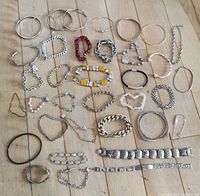 Top down view of 36 costume jewelry bracelets arranged on a wooden surface showing variety of metal bangles, beaded stretch bracelets, chain link bracelets, and decorative cuffs.