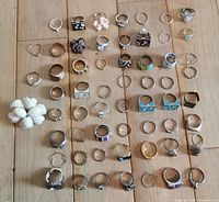 Top-down view of all 59 rings arranged in rows on wooden surface showing variety of designs and colors