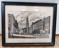 Photo of the framed antique etching or engraving print depicting an urban street scene with a church steeple.