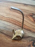 Photo showing side view of small brass mouse figurine with a curved vertical tail on wooden surface.